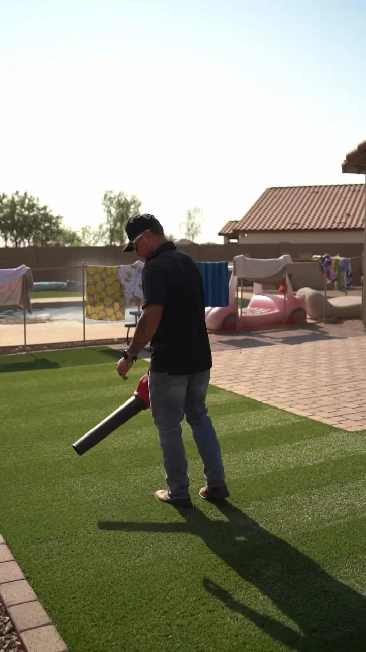 Turf Tune Up technician treating artificial turf in a sunny backyard